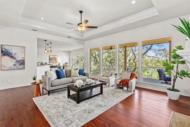 living room with a tray ceiling, baseboards, dark wood-type flooring, and ornamental molding