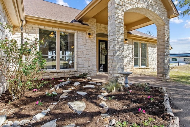 entrance to property featuring stone siding and roof with shingles