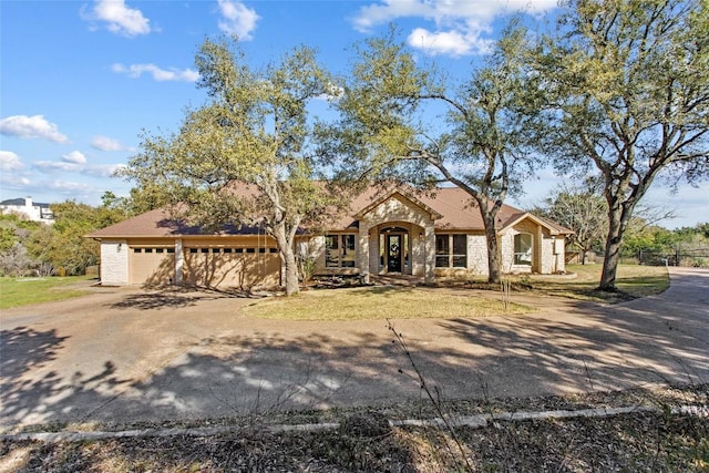 view of front of property featuring driveway, a front lawn, stone siding, fence, and an attached garage