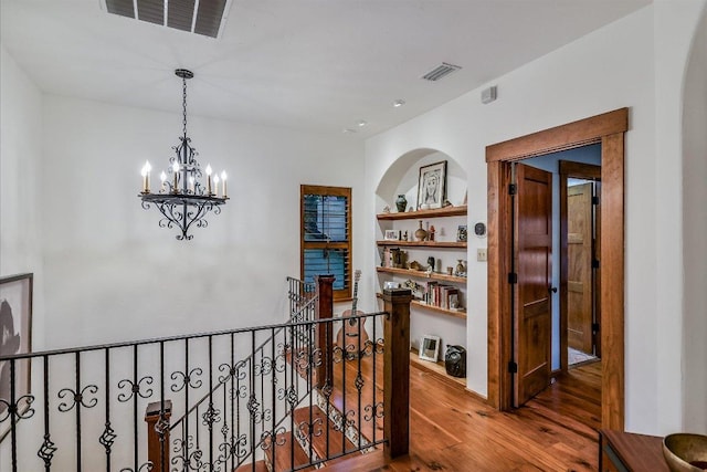 corridor featuring wood finished floors, built in features, an upstairs landing, and visible vents