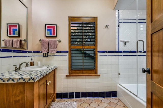 full bathroom featuring vanity, tile walls, a wainscoted wall, and bath / shower combo with glass door