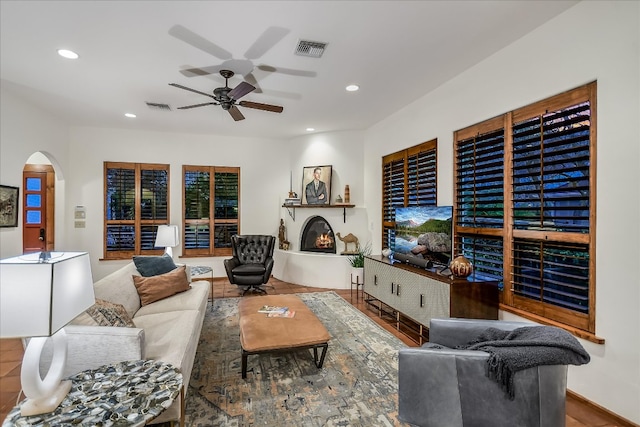 living area featuring arched walkways, visible vents, recessed lighting, and a warm lit fireplace