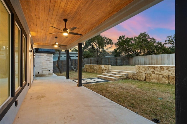 patio terrace at dusk featuring a ceiling fan, a yard, and a fenced backyard