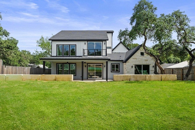 rear view of property featuring a standing seam roof, a yard, a fenced backyard, stone siding, and metal roof