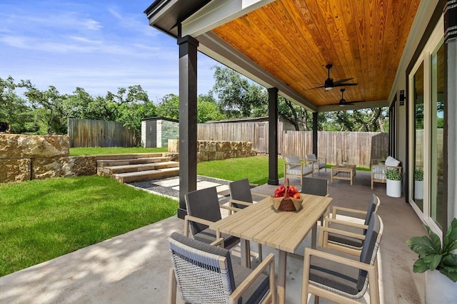 view of patio featuring a storage shed, a fenced backyard, an outdoor structure, outdoor dining space, and a ceiling fan