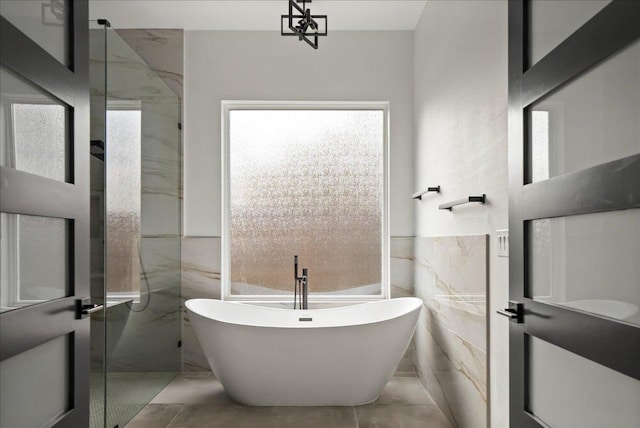 full bathroom with marble finish floor, a freestanding bath, and tile walls