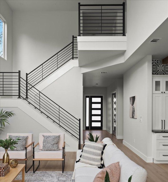 living area with stairway, a high ceiling, visible vents, and wood finished floors