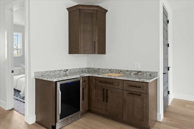 kitchen with dark brown cabinetry, light stone countertops, beverage cooler, and light wood finished floors