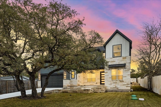 view of front of house featuring board and batten siding, fence, concrete driveway, a lawn, and stone siding