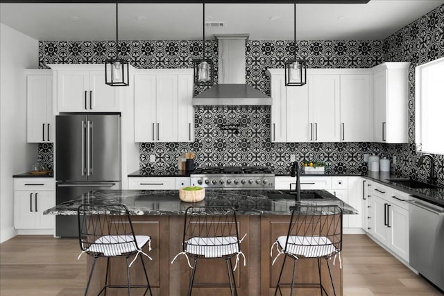 kitchen with a sink, white cabinetry, light wood-style floors, appliances with stainless steel finishes, and wall chimney range hood