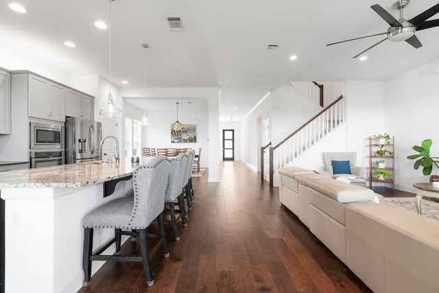 kitchen featuring dark wood-type flooring, ceiling fan, open floor plan, light stone counters, and stainless steel appliances