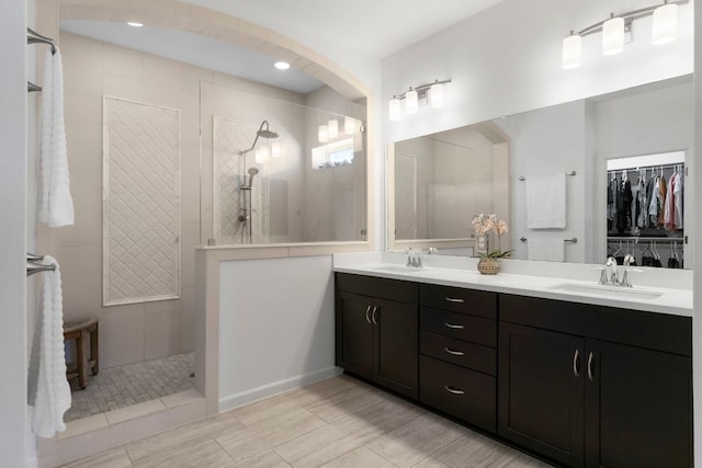 bathroom featuring double vanity, a spacious closet, a walk in shower, and a sink