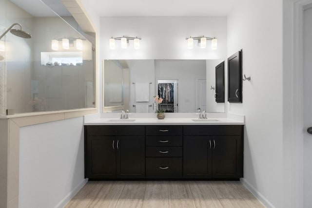 full bath with double vanity, wood finished floors, tiled shower, and a sink