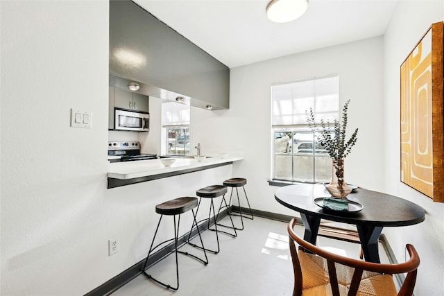 300 Crockett St Unit 118, Austin, TX 78704 - kitchen featuring appliances with stainless steel finishes, a breakfast bar, baseboards, and plenty of natural light