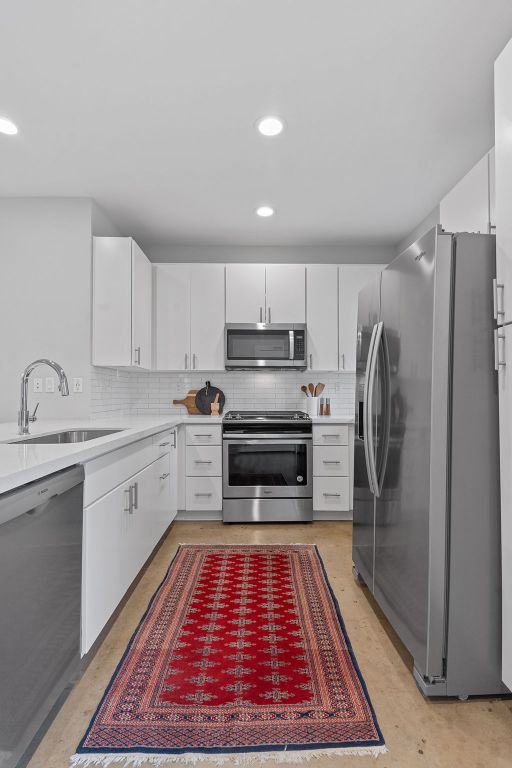 kitchen with a sink, stainless steel appliances, white cabinetry, and light countertops