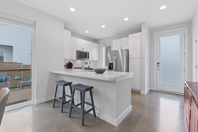 kitchen with a breakfast bar area, recessed lighting, finished concrete floors, appliances with stainless steel finishes, and tasteful backsplash