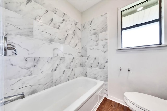 bathroom with toilet, wood finished floors, baseboards, and shower / bathtub combination