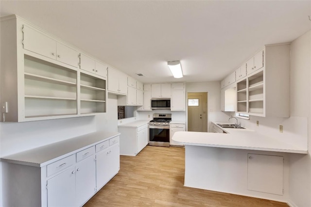 kitchen featuring open shelves, light wood-style flooring, a peninsula, stainless steel appliances, and a sink