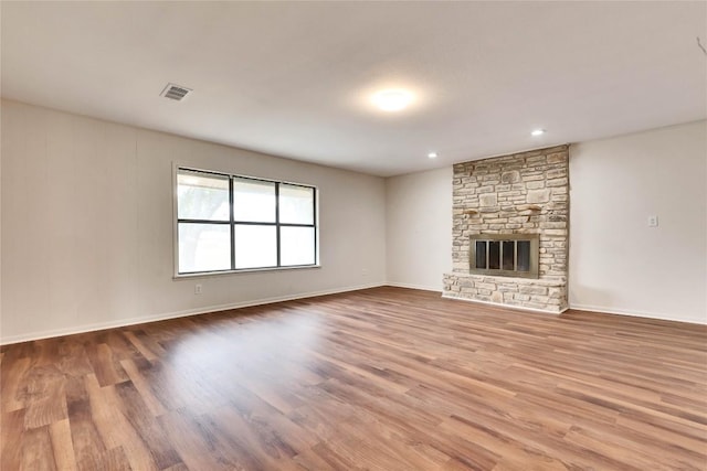 unfurnished living room featuring a stone fireplace, wood finished floors, visible vents, and baseboards