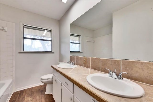 bathroom with toilet, wood finished floors, backsplash, and a sink