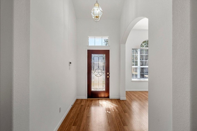 foyer featuring baseboards, arched walkways, wood finished floors, and a towering ceiling