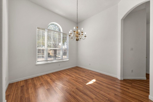 spare room with baseboards, arched walkways, a notable chandelier, and wood finished floors