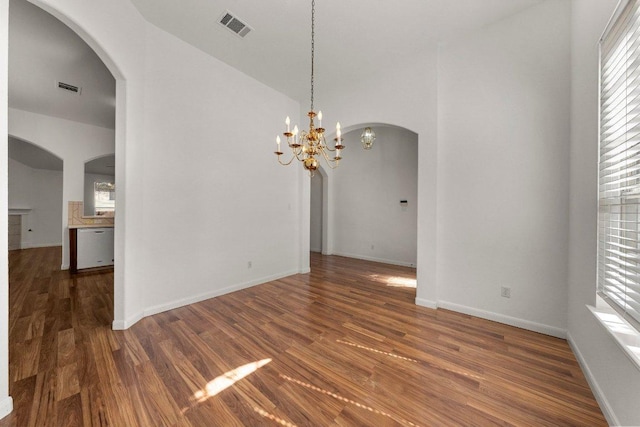 unfurnished room with wood finished floors, baseboards, visible vents, arched walkways, and a chandelier