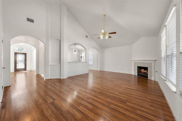 unfurnished living room with visible vents, a tiled fireplace, wood finished floors, arched walkways, and high vaulted ceiling