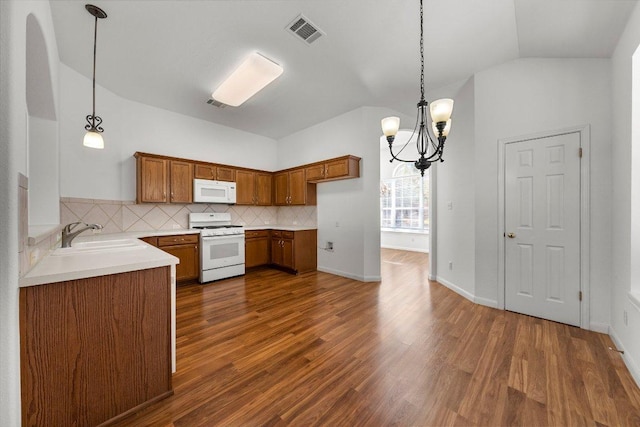 kitchen featuring brown cabinetry, visible vents, white appliances, and a sink