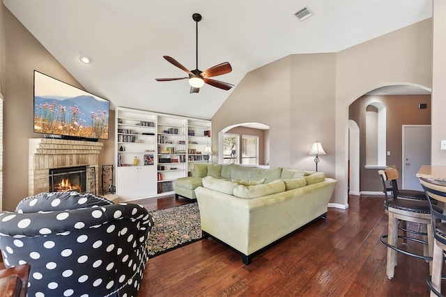 living area with visible vents, arched walkways, wood-type flooring, a brick fireplace, and ceiling fan