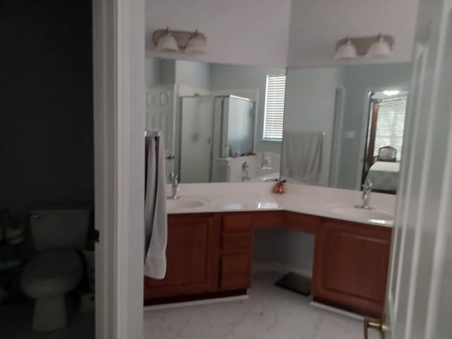 bathroom with a shower stall, toilet, double vanity, marble finish floor, and a sink