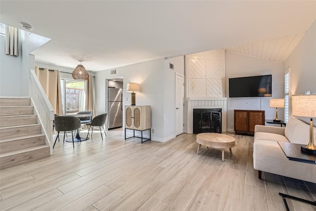 living area featuring visible vents, light wood-style flooring, a fireplace, stairs, and vaulted ceiling