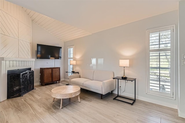 living room with lofted ceiling, a fireplace, baseboards, and light wood finished floors