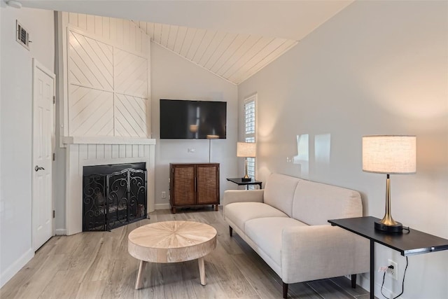 living area featuring lofted ceiling, wood finished floors, a fireplace, and visible vents