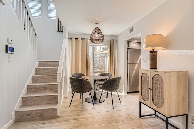 dining room featuring stairway, baseboards, visible vents, and light wood finished floors