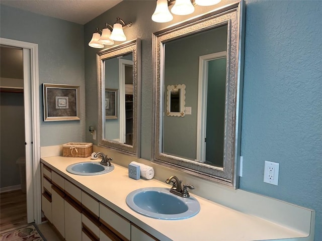 bathroom featuring double vanity, a textured wall, and a sink