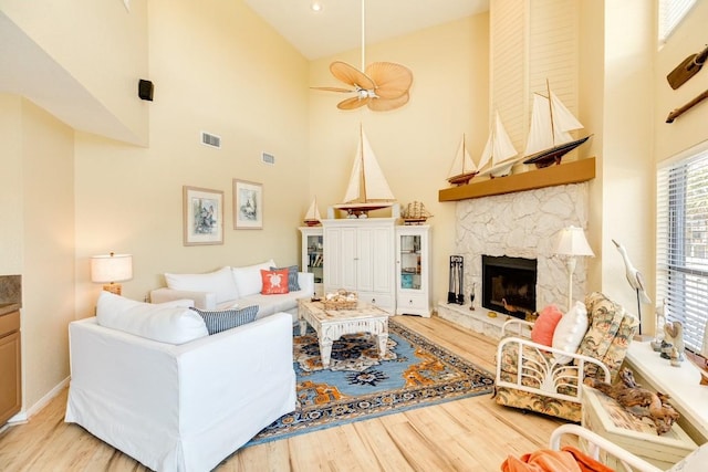 living room featuring visible vents, light wood-style floors, a high ceiling, and a fireplace