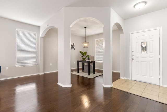 foyer entrance with baseboards, arched walkways, and wood finished floors