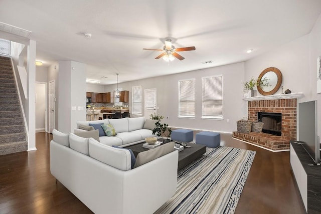 living area featuring dark wood-style floors, a fireplace, stairs, and ceiling fan