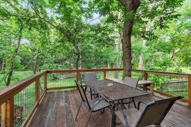 wooden deck with a forest view and outdoor dining space