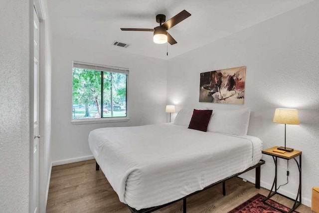 bedroom with ceiling fan, wood finished floors, visible vents, and baseboards