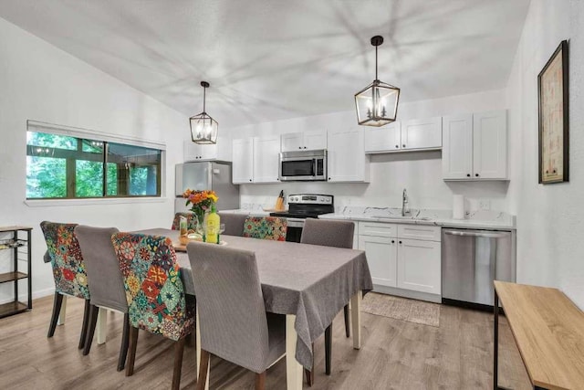 kitchen featuring a sink, stainless steel appliances, white cabinets, light wood-style floors, and decorative light fixtures