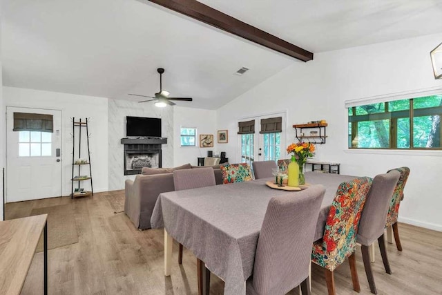 dining area with visible vents, light wood-style flooring, lofted ceiling with beams, a fireplace, and ceiling fan