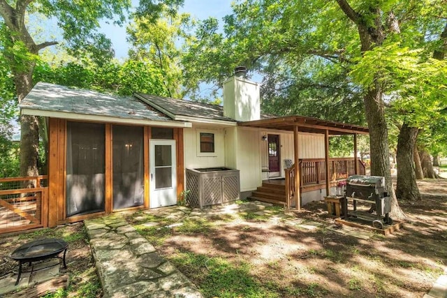 rear view of house featuring a wooden deck, a chimney, and a sunroom