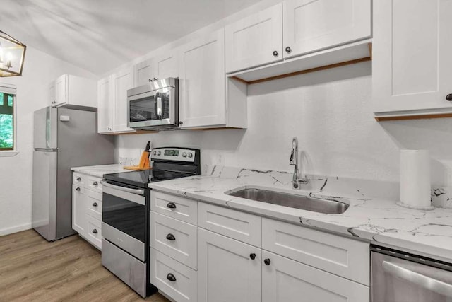 kitchen featuring light stone counters, light wood finished floors, a sink, stainless steel appliances, and white cabinetry