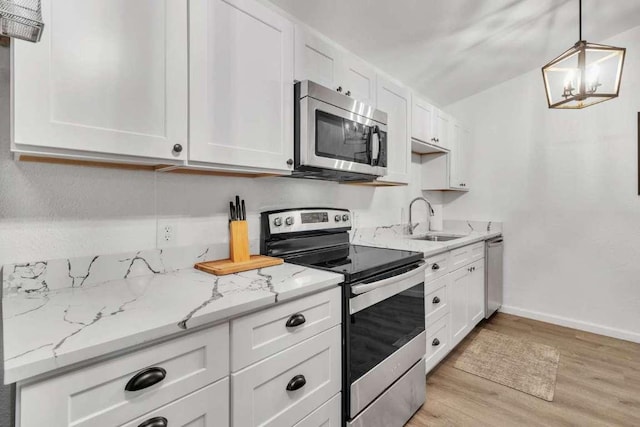 kitchen with light stone countertops, light wood-style flooring, a sink, white cabinets, and appliances with stainless steel finishes