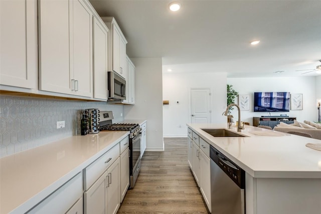 kitchen with a sink, tasteful backsplash, wood finished floors, recessed lighting, and appliances with stainless steel finishes