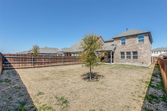 rear view of house featuring brick siding, a yard, and a fenced backyard