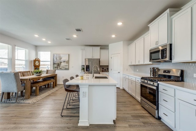 kitchen featuring visible vents, a sink, stainless steel appliances, light wood-style floors, and light countertops