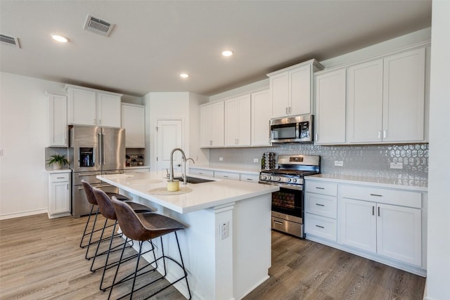 kitchen featuring visible vents, a breakfast bar, light wood-type flooring, stainless steel appliances, and a sink